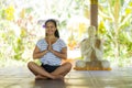 Young beautiful and happy Asian Indonesian woman with Balinese style ear flower sitting on wood floor in lotus pose smiling at Royalty Free Stock Photo