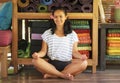 Young beautiful and happy Asian Indonesian woman sitting on wood floor in lotus pose smiling at yoga studio relaxed and zen like Royalty Free Stock Photo