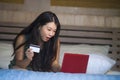 Young beautiful happy Asian Japanese girl using credit card internet banking on laptop computer at home in bed shopping online e-c