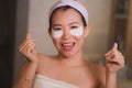 Young beautiful and happy Asian Japanese woman smiling to bathroom mirror applying hydrating eye patches under the eyes in beauty Royalty Free Stock Photo