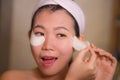 Young beautiful and happy Asian Japanese woman smiling to bathroom mirror applying hydrating eye patches under the eyes in beauty Royalty Free Stock Photo