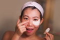 Young beautiful and happy Asian Japanese woman smiling to bathroom mirror applying hydrating eye patches under the eyes in beauty Royalty Free Stock Photo