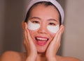 Young beautiful and happy Asian Japanese woman smiling to bathroom mirror applying hydrating eye patches under the eyes in beauty Royalty Free Stock Photo
