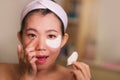 Young beautiful and happy Asian Japanese woman smiling to bathroom mirror applying hydrating eye patches under the eyes in beauty Royalty Free Stock Photo