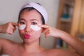 Young beautiful and happy Asian Japanese woman smiling to bathroom mirror applying hydrating eye patches under the eyes in beauty Royalty Free Stock Photo