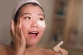 Young beautiful and happy Asian Japanese woman smiling to bathroom mirror applying hydrating eye patches under the eyes in beauty Royalty Free Stock Photo