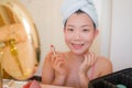 Young beautiful and happy Asian Japanese woman with towel head wrap applying makeup looking to mirror smiling cheerful preparing Royalty Free Stock Photo