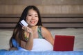 Young beautiful happy Asian Japanese woman using credit card internet banking on laptop computer at home in bed shopping online e- Royalty Free Stock Photo