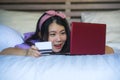 Young beautiful happy Asian Japanese woman using credit card internet banking on laptop computer at home in bed smiling shopping o Royalty Free Stock Photo
