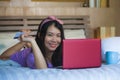 Young beautiful happy Asian Japanese woman using credit card internet banking on laptop computer at home in bed smiling shopping o Royalty Free Stock Photo