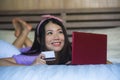 Young beautiful happy Asian Japanese woman using credit card internet banking on laptop computer at home in bed smiling shopping o Royalty Free Stock Photo