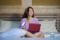 Young beautiful happy Asian Japanese woman using credit card internet banking on laptop computer at home in bed smiling shopping o Royalty Free Stock Photo