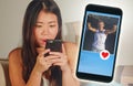 Young beautiful and happy Asian Korean girl using internet online dating app on mobile phone sending like message to handsome Cauc