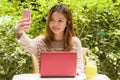 Young beautiful and happy Asian Chinese student girl sitting at coffee shop garden working with laptop computer taking selfie Royalty Free Stock Photo