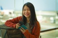 Young beautiful and happy Asian Korean woman checking mobile phone holding passport in her hand at airport departure lounge Royalty Free Stock Photo