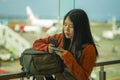 Young beautiful and happy Asian Korean woman checking mobile phone holding passport in her hand at airport departure lounge Royalty Free Stock Photo