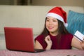 Young beautiful and happy Asian Korean woman in Christmas Santa Claus hat holding credit card using laptop computer for internet o Royalty Free Stock Photo