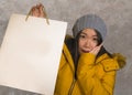 Young beautiful and happy Asian Korean woman in cool winter hat holding shopping bag excited buying Christmas present smiling Royalty Free Stock Photo