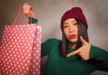 Young beautiful and happy Asian Korean woman in cool winter hat holding shopping bag excited buying Christmas present smiling in Royalty Free Stock Photo