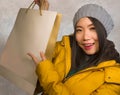 Young beautiful and happy Asian Korean woman in cool winter hat holding shopping bag excited buying Christmas present smiling Royalty Free Stock Photo