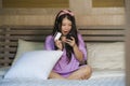 Young beautiful and happy Asian Korean woman at home bedroom using credit card internet banking with mobile phone in bed smiling o Royalty Free Stock Photo