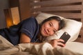 Young beautiful and happy Asian Korean woman in pajamas using mobile phone social media texting with her boyfriend or enjoying Royalty Free Stock Photo