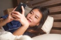 Young beautiful and happy Asian Korean woman in pajamas using mobile phone social media texting with her boyfriend or enjoying Royalty Free Stock Photo