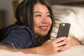 Young beautiful and happy Asian Korean woman in pajamas using mobile phone social media texting with her boyfriend or enjoying Royalty Free Stock Photo