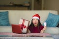 Young beautiful and happy Asian Korean woman in Santa hat holding credit card and Christmas present box using laptop computer for Royalty Free Stock Photo