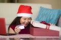 Young beautiful and happy Asian Korean woman in Santa hat holding credit card and Christmas present box using laptop computer for Royalty Free Stock Photo