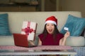 Young beautiful and happy Asian Korean woman in Santa hat holding credit card and Christmas present box using laptop computer for Royalty Free Stock Photo