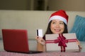 Young beautiful and happy Asian Korean woman in Santa hat holding credit card and Christmas present box using laptop computer for Royalty Free Stock Photo