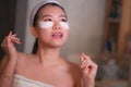 Young beautiful and happy Asian Korean woman smiling to bathroom mirror applying hydrating eye patches under the eyes in beauty Royalty Free Stock Photo