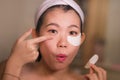 Young beautiful and happy Asian Korean woman smiling to bathroom mirror applying hydrating eye patches under the eyes in beauty Royalty Free Stock Photo