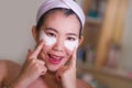 Young beautiful and happy Asian Korean woman smiling to bathroom mirror applying hydrating eye patches under the eyes in beauty Royalty Free Stock Photo