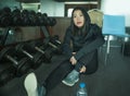 Young beautiful and happy Asian Korean woman in sport hoodie posing cool at fitness center sitting by dumbbells rack during Royalty Free Stock Photo