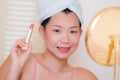 Young beautiful and happy Asian Korean woman with towel head wrap applying makeup looking to mirror smiling cheerful preparing for Royalty Free Stock Photo