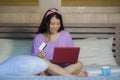 Young beautiful happy Asian Korean woman using credit card internet banking on laptop computer at home in bed smiling shopping onl Royalty Free Stock Photo