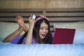 Young beautiful happy Asian Korean woman using credit card internet banking on laptop computer at home in bed smiling shopping onl Royalty Free Stock Photo