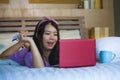 Young beautiful happy Asian Korean woman using credit card internet banking on laptop computer at home in bed smiling shopping onl Royalty Free Stock Photo