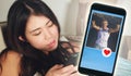 Young beautiful and happy Asian Korean woman using internet online dating app on mobile phone sending like message to handsome Cau Royalty Free Stock Photo