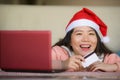 Young beautiful and happy Asian Korean woman wearing Santa hat holding credit card and Christmas present box using laptop computer Royalty Free Stock Photo