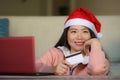 Young beautiful and happy Asian Korean woman wearing Santa hat holding credit card and Christmas present box using laptop computer Royalty Free Stock Photo