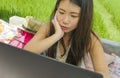 Young beautiful and happy Asian Korean woman working outdoors with laptop computer networking green grass background cafe as digit Royalty Free Stock Photo