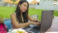 Young beautiful and happy Asian Korean woman working outdoors with laptop computer networking green grass background cafe as digit Royalty Free Stock Photo