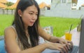 Young beautiful and happy Asian Korean woman working outdoors with laptop computer networking green grass background cafe as digit Royalty Free Stock Photo