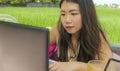 Young beautiful and happy Asian Korean woman working outdoors with laptop computer networking green grass background cafe as digit Royalty Free Stock Photo