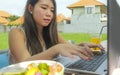 Young beautiful and happy Asian Korean woman working outdoors with laptop computer networking green grass background cafe as digit Royalty Free Stock Photo