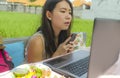 Young beautiful and happy Asian Korean woman working outdoors with laptop computer networking green grass background cafe as digit Royalty Free Stock Photo
