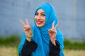 Young beautiful and happy Asian woman in hijab muslim head scarf posing to the camera playful having fun doing success victory V s Royalty Free Stock Photo